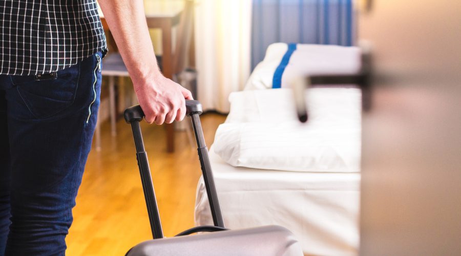 Man pulling suitcase and entering hotel room. Traveler going in to room or walking inside motel with luggage.